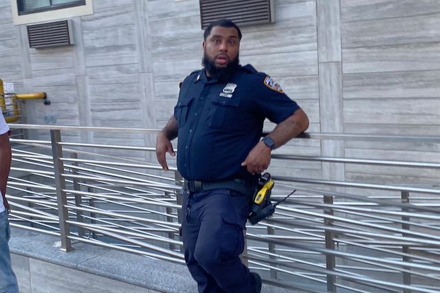 An officer stands on a NYC sidewalk without a mask.